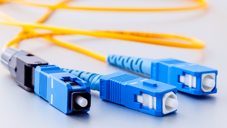 Close-up of three blue SC fiber-optic connectors attached to yellow fiber cables, resting on a light-colored surface.