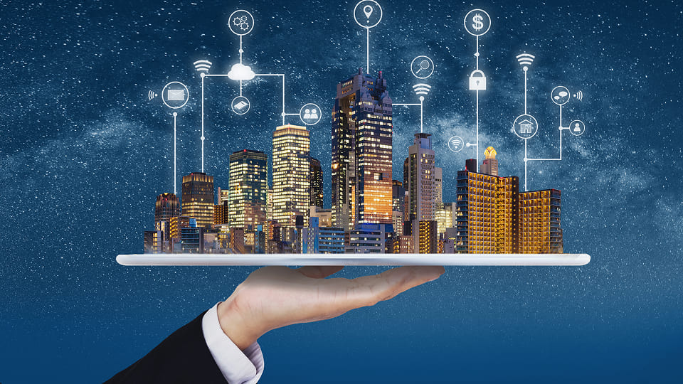 Hand holding tablet with illuminated smart city skyline and digital connectivity icons in a starry night sky.