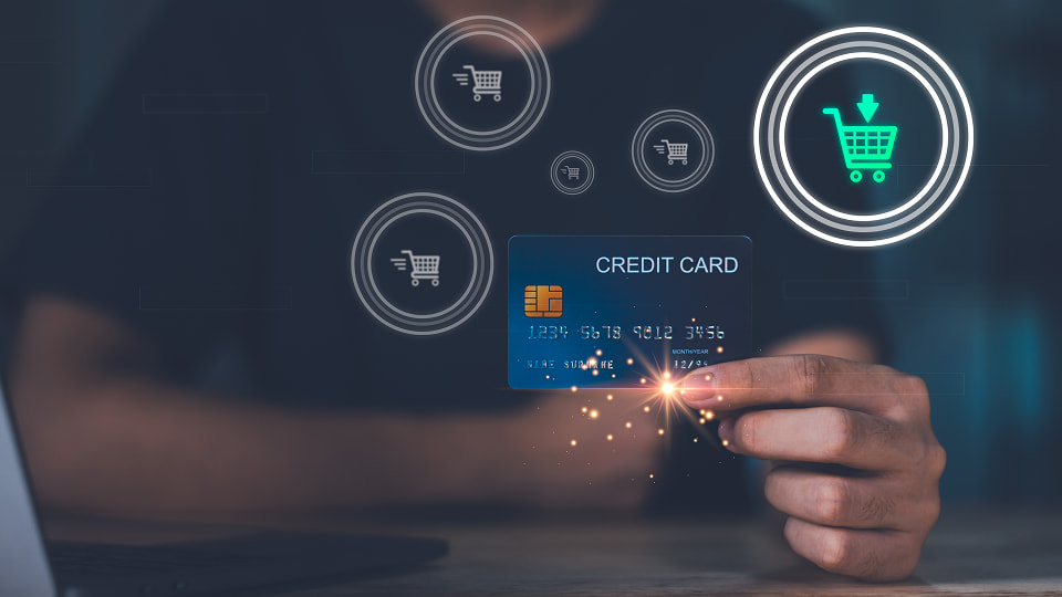 Person holding credit card with digital shopping cart icons, representing online payment and e-commerce transaction.