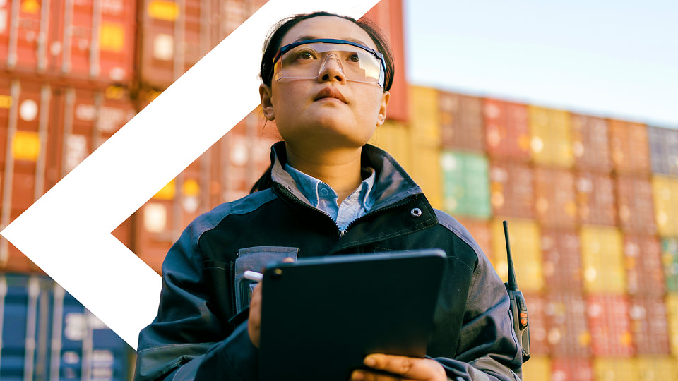 Female logistics worker inspecting cargo containers with tablet and radio communication device.